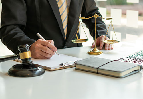 Lawyer signing legal paperwork with scales of justice and gavel on desk.