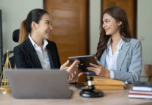 Two professional women discussing legal matters over a laptop and tablet.